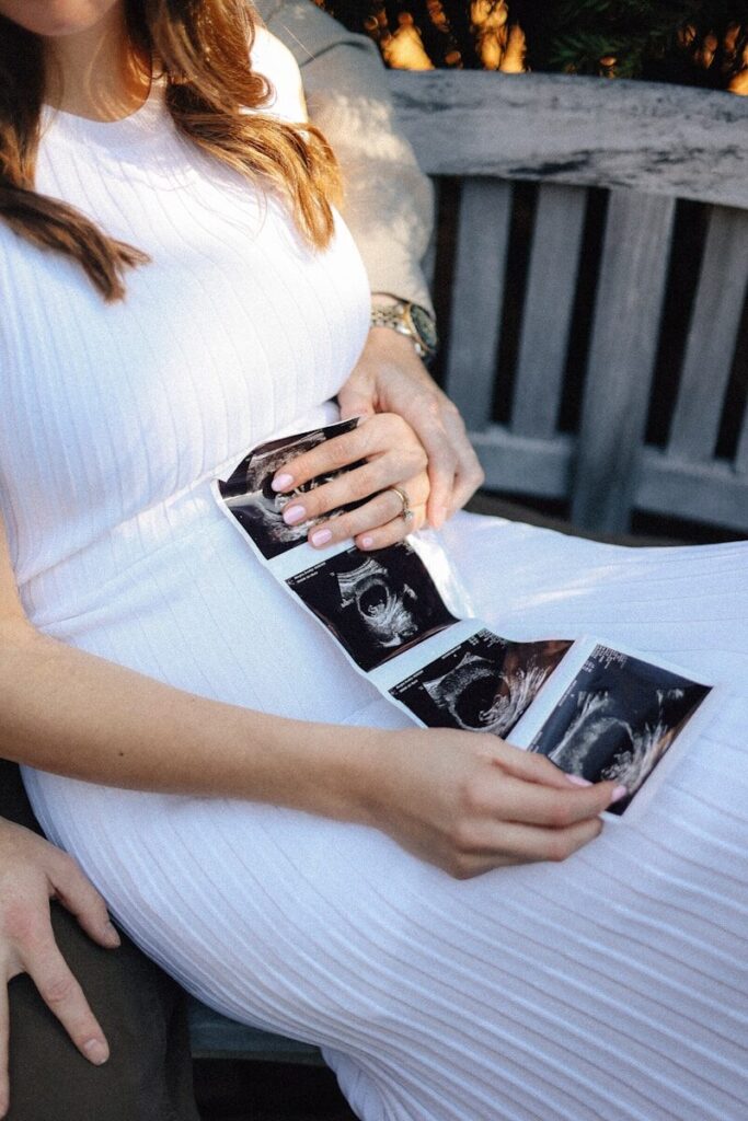 A pregnant woman quietly holds a strip of ultrasound photos on her lap.