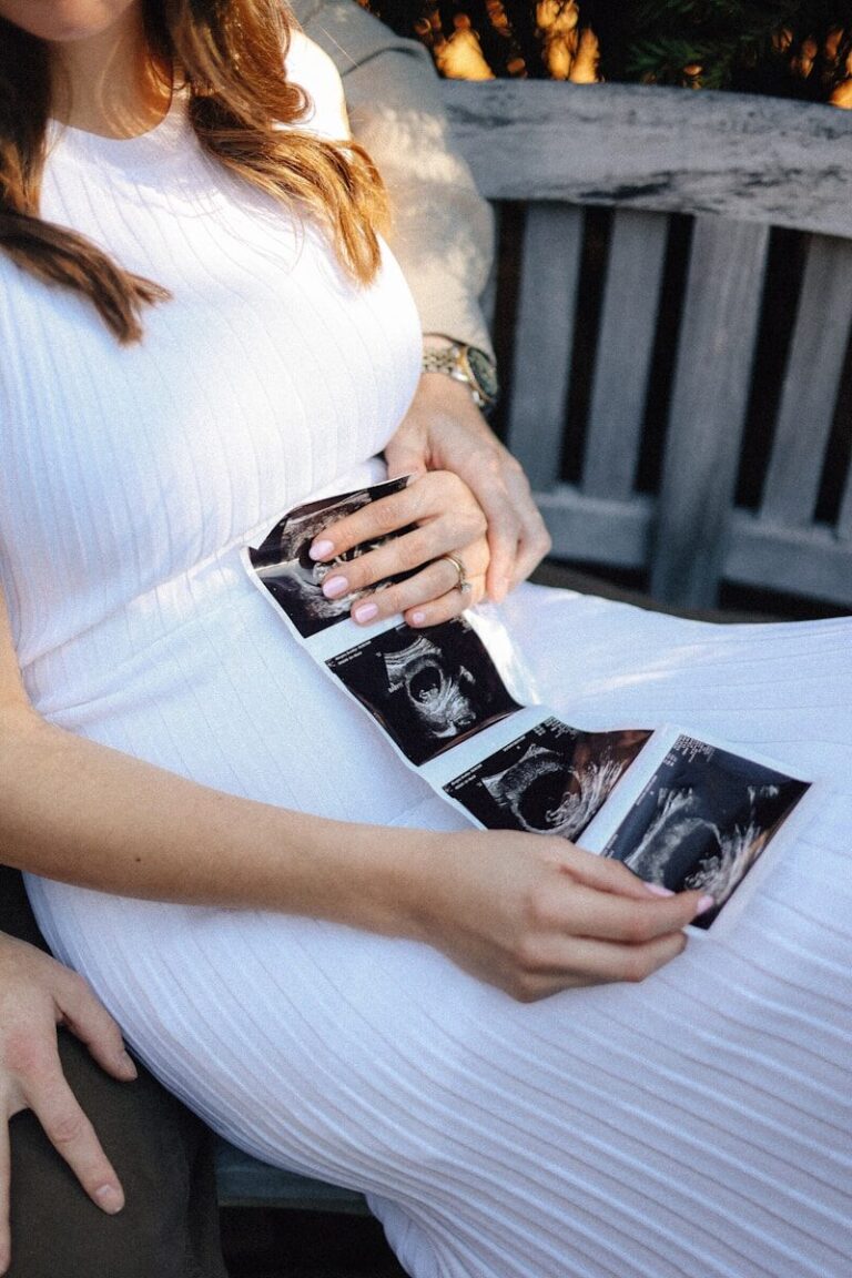 A pregnant woman quietly holds a strip of ultrasound photos on her lap.