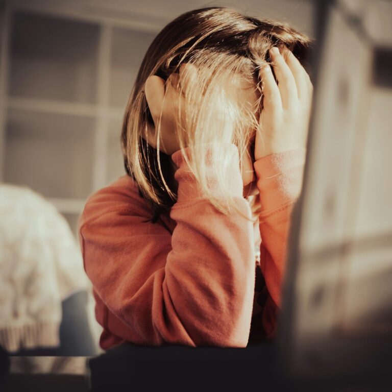 A woman in a rust-colored sweater presses her hands to her face in frustration.