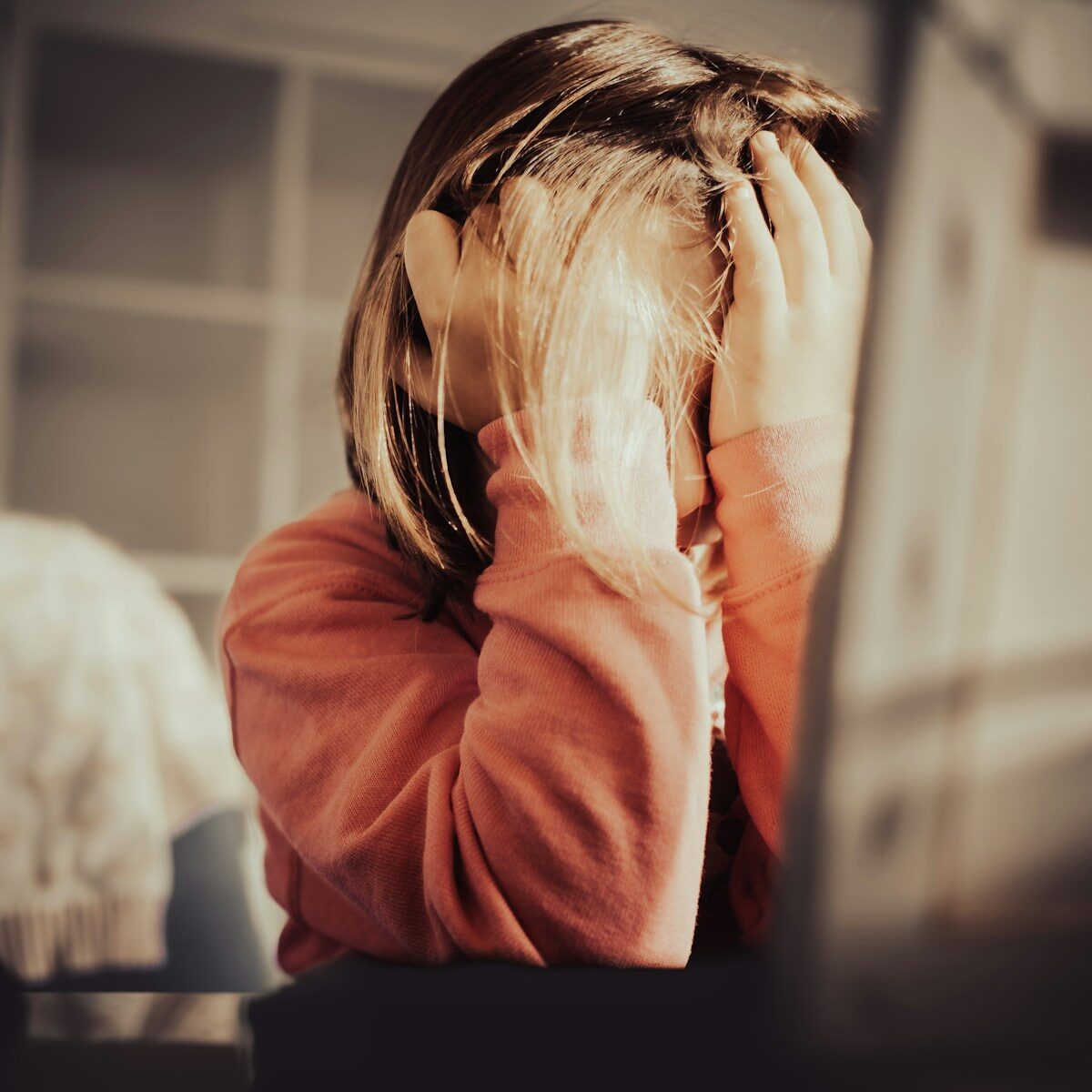 A woman in a rust-colored sweater presses her hands to her face in frustration.