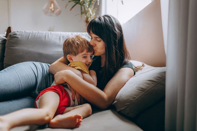 A tired mother rests on the couch while her young son curls up against her.