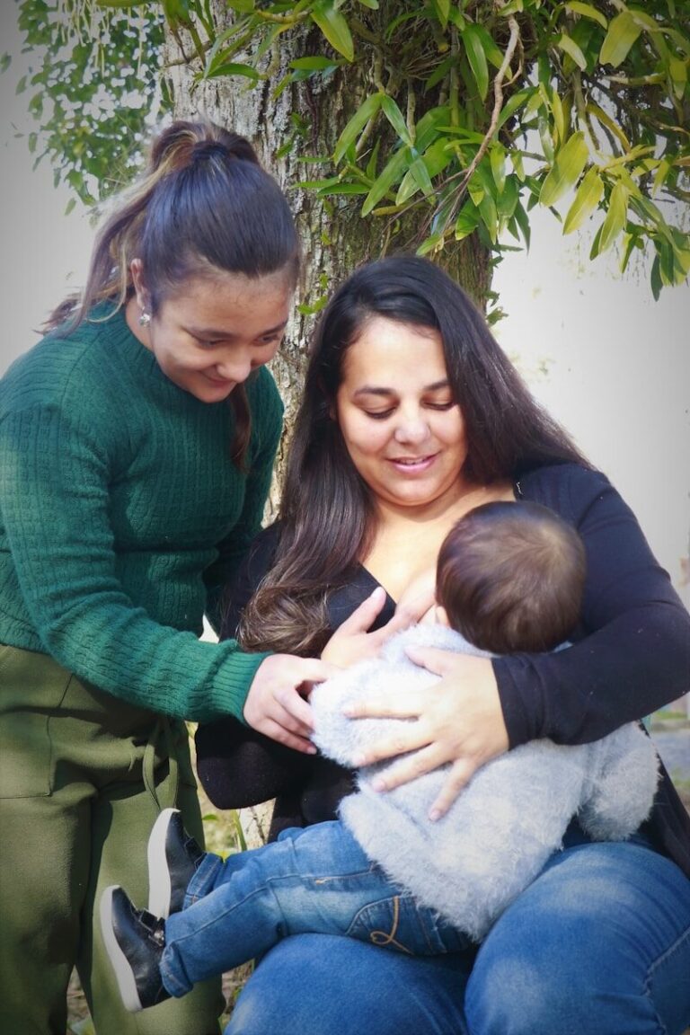 Two mothers lean close together while one of them feeds their baby.